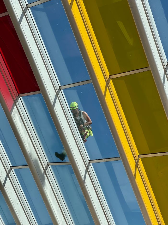 services-02 High-angle view of a worker cleaning a vibrant glass roof, featuring red, blue, and yellow panels.